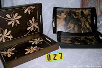 Two sets of wood serving trays on a blue-gray patterned surface, each set with large and smaller tray. Front set is floral inlaid design, back set has angel artwork.