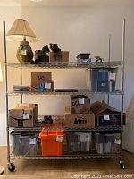 First rolling metal shelf fully assembled, loaded with boxes and household items, standing on caster wheels.