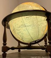 Close-up photo showing the illuminated antique globe mounted on a dark wooden frame with turned legs and feet, globe lit internally.