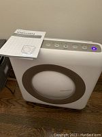 Photo showing Coway HEPA air purifier with control panel on top and instruction manual leaning against it.