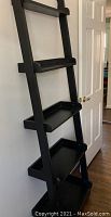 Full view of black wooden leaning bookcase showing all 5 shelves and side supports