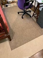 Tan and brown woven rectangular throw rug laid on floor under office chair and beside bed.