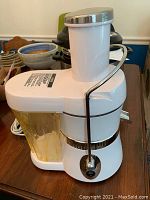 Side angled view of white Jack LaLanne juicer, showing clear yellow juice container and safety latch on side.