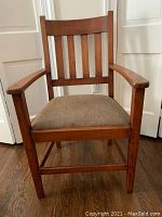 Front view of Mission style wooden arm chair showing vertical slats on backrest and cushioned seat in beige upholstery