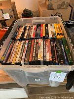 Photo of DVDs arranged vertically in a clear plastic bin showing multiple titles with visible cover art and labels.