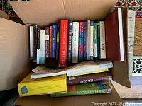 Mixed lot of books in a box with spines clearly visible showing titles and authors.
