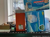 Photo of boxes of humidifiers including Vicks and Walmart brands stacked on a black surface to show the lot includes multiple humidifiers