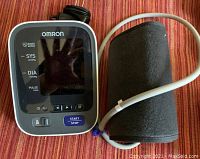 Front view of Omron blood pressure monitor with attached arm cuff and power adapter cord.