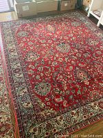 Full view of the antique Oriental carpet with red background and floral patterns in living room setting.