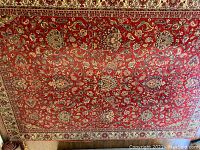 Full view of rectangular oriental carpet with red field and floral patterns covering the main surface, bordered with a detailed floral cream band.