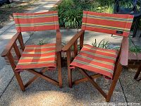 Pair of wooden folding directors chairs with removable orange Kenyan kikoy fabric seats and backrests placed outdoors on a stone patio.
