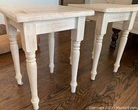 Pair of square wooden side tables with turned legs in a distressed white paint finish, shown on a hardwood floor.