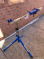 Full side view of the Park Tool bicycle repair stand showing the blue tripod legs and adjustable clamps on the horizontal bar.