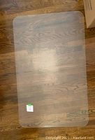 Image showing the flat rectangular clear plastic floor protector on a wood floor with gentle reflections from lighting.