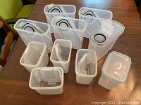 Overview photo showing 5 large and 5 small clear plastic food containers with white snap-lock lids arranged on table.