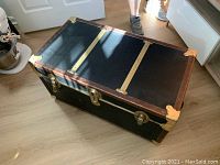 Top view of black rolling storage trunk showing brass bands and corner protectors