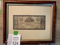 Framed South Carolina Confederate $20 bill laid on wooden surface with auction lot number tag visible