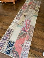Full length view of a Turkish runner rug on wooden floor showing patchwork design with varied traditional carpet motifs in reds, blues, beiges, greens.