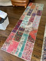 Full view of long Turkish runner rug with patchwork pattern and varied colorful designs placed on a wooden floor.