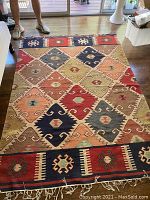 Full view of Turkish wool rug laid out on wooden floor, showing colorful geometric patterns and distinct borders with fringe.