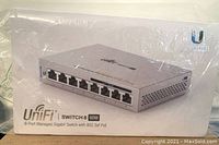 Photo of sealed UniFi Switch 8 60W packaging showing image of the device with 8 Ethernet ports and Ubiquiti branding.