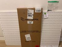 Two white pegboard panels positioned behind a large brown box labeled Wall Control 30-P-3232W, indicating one set still boxed.