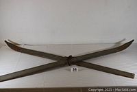 Pair of vintage wood skis crossed on a white surface, showing full length and leather bindings.
