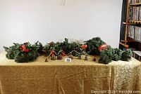 Full view of all sleigh bells and evergreen garlands laid on a gold cloth background showing sizes and layout.