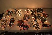 Photo showing 18 bundled strings of Christmas lights in multicolor and white, laid on a flat surface with some illuminated.