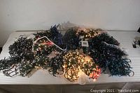 View of all 20 tangled strings of Christmas lights, mostly blue, multicolor, and white, lying on a white surface.