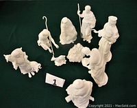 View of all 10 white porcelain nativity figures on dark green surface showing arrangement of Holy Family, shepherds, wise men, and lamb.