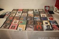 Full lot displayed on table showing 40+ Christmas and holiday music CDs arranged in rows with a red and white crate at side, with pen and calculator visible.