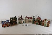 Photo showing all six ceramic houses lined up from left to right, including a dairy barn with silo, town hall, church, Victorian house, elementary school, and post office all lit internally.