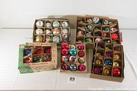 Five trays/boxes of assorted vintage Christmas ornaments displayed together on white surface.