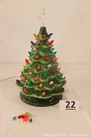 Front view of green ceramic Christmas tree with colorful plastic lights attached on branches. Small extra lights placed beside the tree.