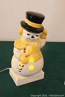 Front and side views of vintage ceramic snowman with yellow scarf, black top hat, and lighted buttons.