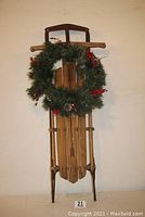 Full view of vintage wooden sled standing upright with green Christmas wreath attached to front.