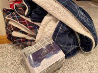 Two plaid throw blankets folded to show lining and patterns alongside the LOFTEX hand towel set still packaged.