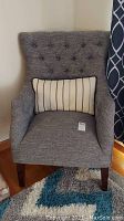 Front view of gray upholstered accent chair with tufted back and striped pillow on seat.