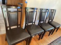 Six dark wood dining chairs with upholstered dark seats, arranged in a row on a wood floor.