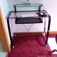 Front view of computer desk showing tempered glass surfaces, metal frame, and caster wheels