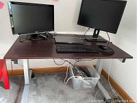 Full view of adjustable height desk showing top, two computer monitors, keyboard and mouse on its surface and casters below.