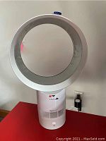 Front view of Dyson Cool AM06 fan on red surface with power outlet in background