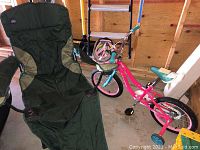 Photo shows a green and black Mac folding sports chair and a pink and blue kids bicycle with training wheels, both placed indoors on concrete floor
