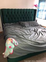 Full view of the king size upholstered bed frame with tufted wingback headboard and nailhead trim, dressed with bedding sheets and pillow.