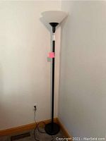 Full view of the floor lamp showing black metal base, pole and white plastic shade.