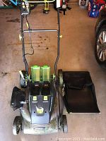 Full side and front view of Earthwise electric lawn mower with two translucent green battery compartments and detachable black leaf bag on the floor next to it