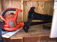 Black & Decker electric leaf blower with detachable blower tube attachment placed on wooden shelf.