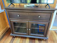 Front view of media console showing drawer and two glass doors with contents not included