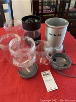 Photo showing NutriBullet blender base, multiple clear plastic containers and matching lids on red tablecloth.